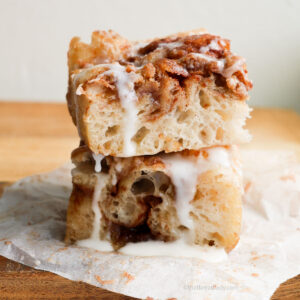 Two slices of cinnamon roll focaccia stacked on a wood bread board.