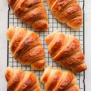 6 croissants on a wire cooling rack.
