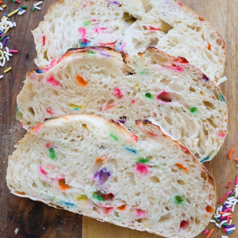 Three slices of funfetti sourdough bread on a wood cutting board.