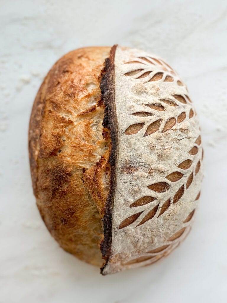 A loaf of sourdough scored with wheat stalks on one side.