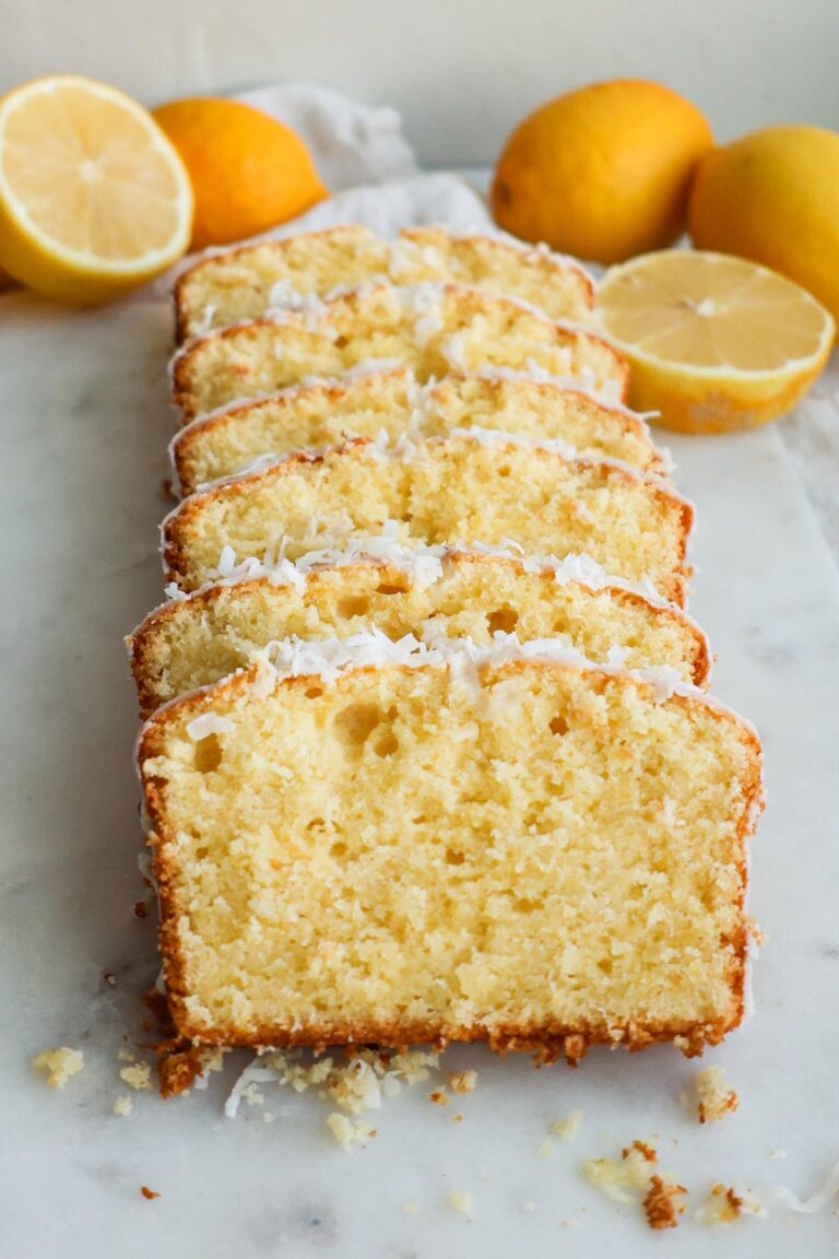 Lemon coconut bread, sliced on a white marble cutting board with lemons around it.