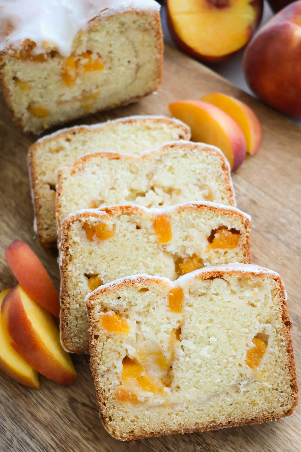 Peach bread sliced and placed on a wood cutting board with peach slices around it.