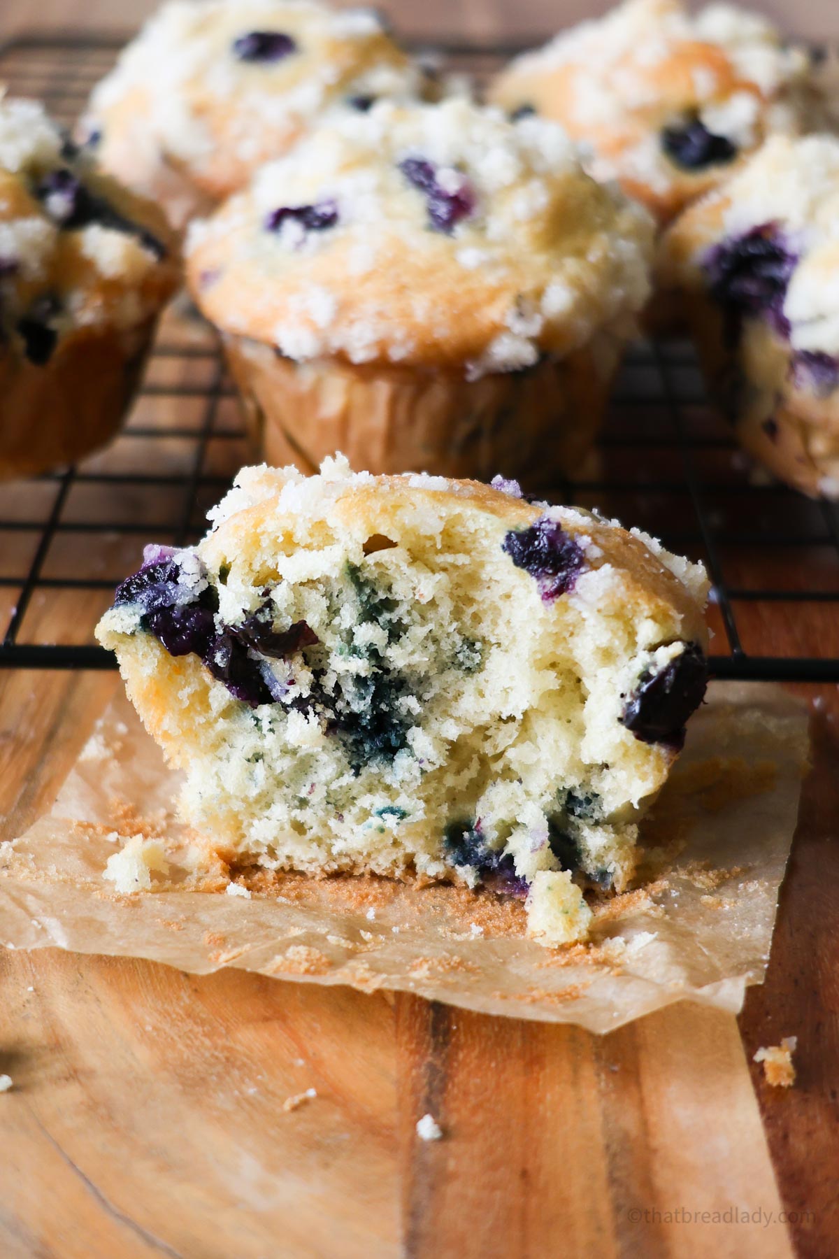 A sourdough blueberry muffin cut in half with more blueberry muffins in the background.