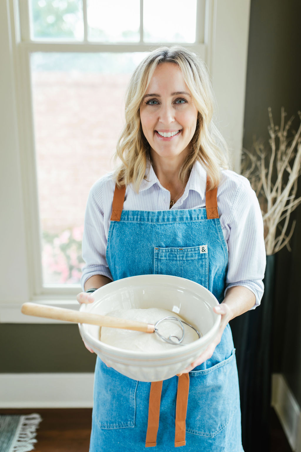 Woman standing with a bowl of bread dough and a danish whisk inside the bowl.