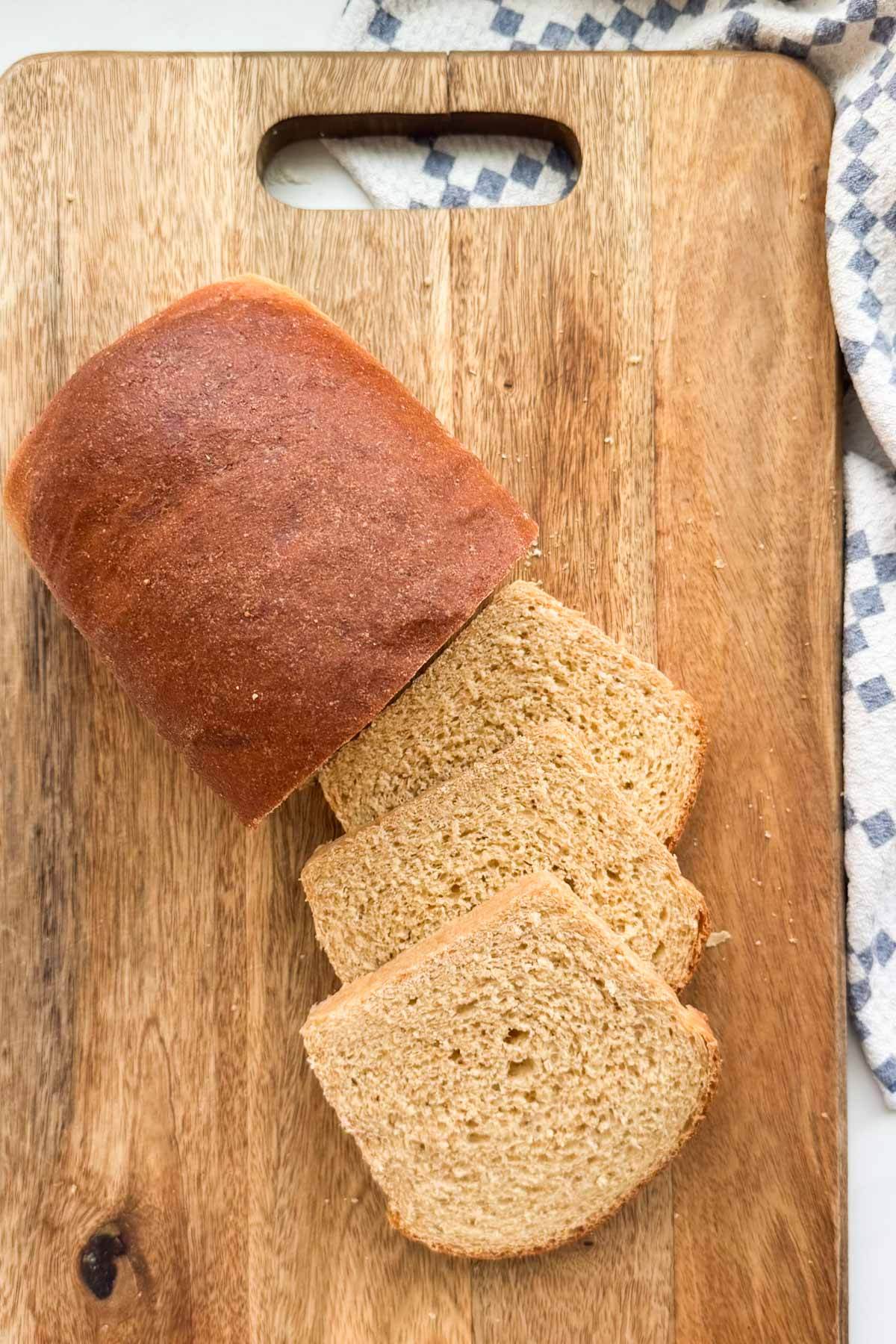 A loaf of honey whole what bread, sliced on a wood bread board.